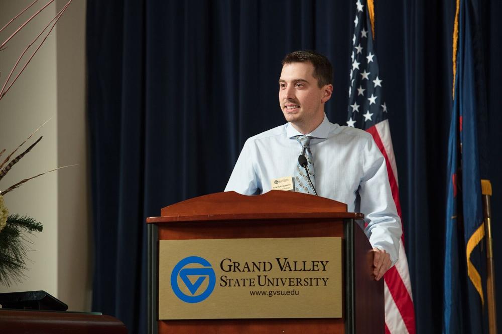A man standing at a GVSU podium, speaking to the crowd